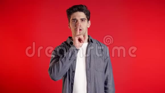 欧洲英俊的男人用手指在红色背景上的嘴唇上手势秘密沉默视频的预览图