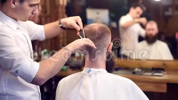 男士理发店用剪刀剪发弯着腰的男客户坐在后面镜面反射模糊视频的预览图