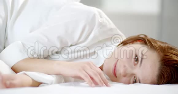 微笑的幸福女人穿着白色衬衫躺在床上闭上眼睛4K视频的预览图