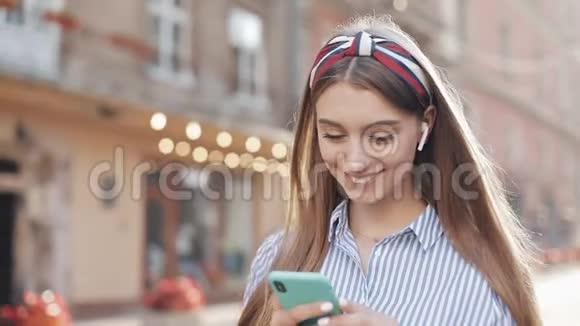 年轻美丽的女孩棕色头发时尚头巾穿着条纹衬衫和耳机使用智能手机视频的预览图