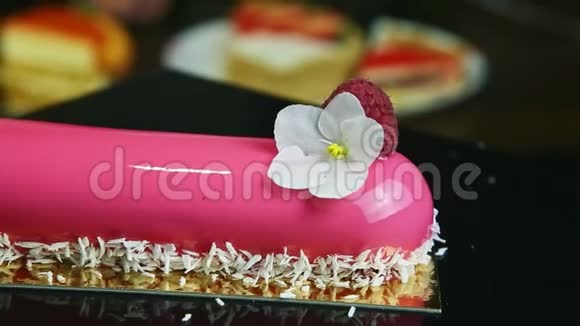 黑色支架上有花和覆盆子的粉色釉色椭圆蛋糕视频的预览图
