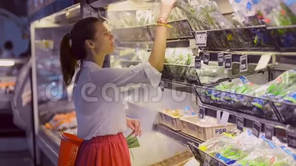 年轻的素食妇女闻着选择绿色蔬菜站在有机商店视频的预览图