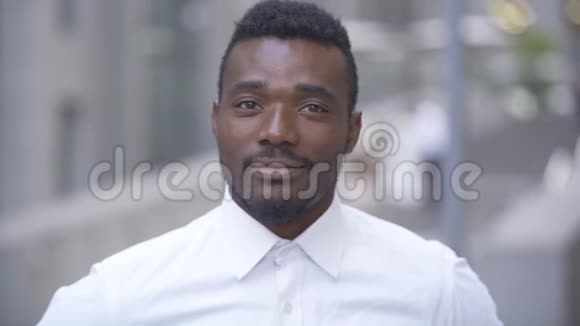一位身穿白色衬衫站在城市里看镜头的英俊微笑非裔美国人的特写视频的预览图
