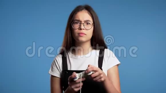 漂亮的亚洲女孩在电视上玩电子游戏在蓝色工作室墙上的操纵杆利用现代技术视频的预览图