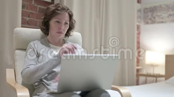 老妇人在卧室里思考和工作笔记本电脑视频的预览图