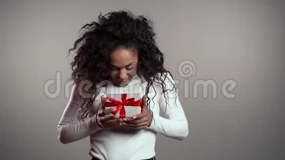 惊讶的混血女人微笑拿着礼品盒在灰色工作室背景视频的预览图