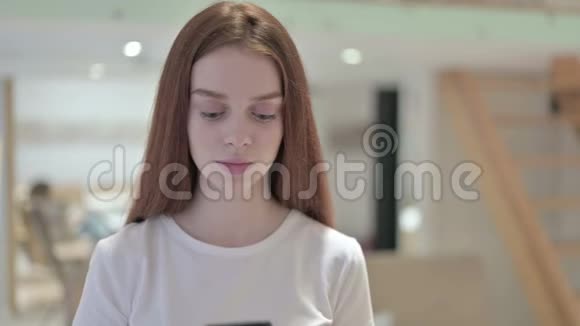 开朗的红头发青年妇女在智能手机上讲话的肖像视频的预览图