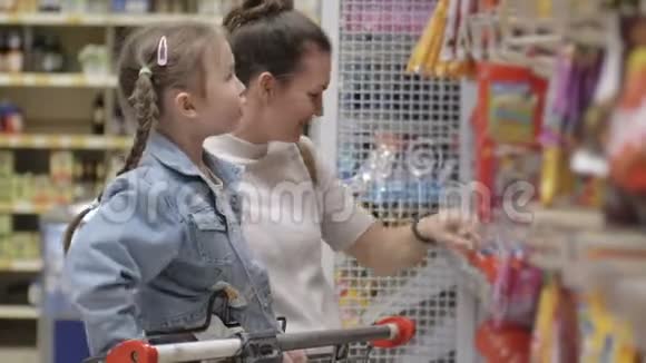 美丽的女人带着女儿在超市购物年轻的母亲在超市为孩子选择食物和糖果视频的预览图
