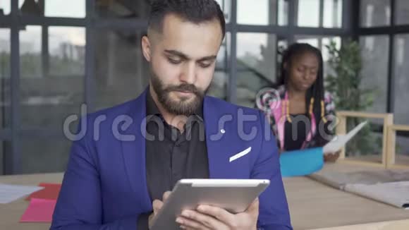 白人男子在平板电脑的前景上看照片而非裔美国女设计师则在查看文件视频的预览图