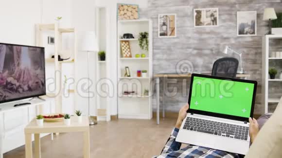 一个男人躺在客厅的沙发上手里拿着一台绿色屏幕笔记本电脑视频的预览图
