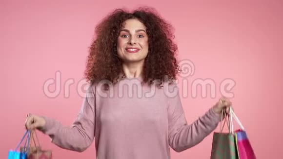 一位年轻快乐的女士购物后带着五颜六色的纸袋与粉红色隔离开来视频的预览图