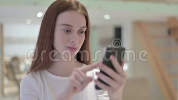 红发青年妇女庆祝智能手机成功的肖像视频的预览图