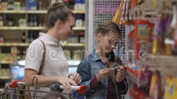 美丽的布鲁内特女士与女儿站在货架附近与货物幸福家庭选择产品视频的预览图