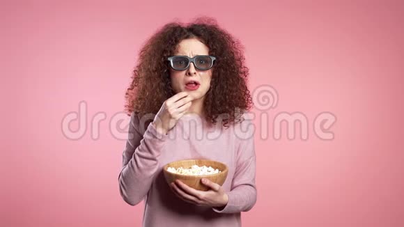 戴着3d眼镜看恐怖电影的年轻女子在粉红工作室吃爆米花视频的预览图