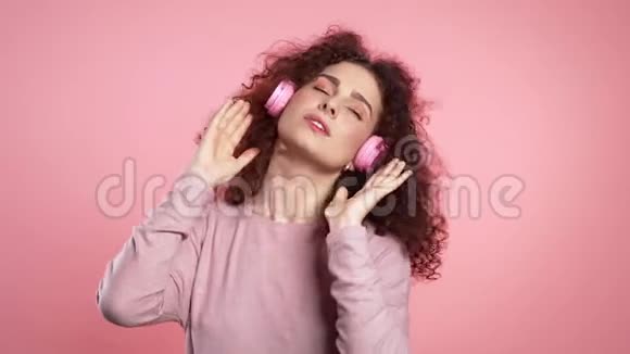 一位留着卷发戴着耳机跳舞的漂亮女士她在粉色工作室跳舞视频的预览图