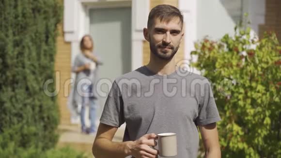 英俊的白种人男子站在前台端着茶杯看着镜头女孩站在后台视频的预览图