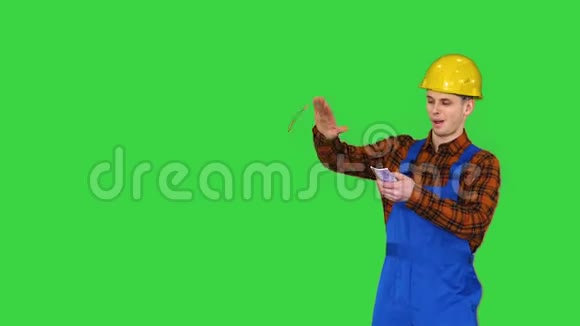 施工工人戴着黄色安全帽把钱扔到空中放在绿色的屏幕上铬钥匙视频的预览图