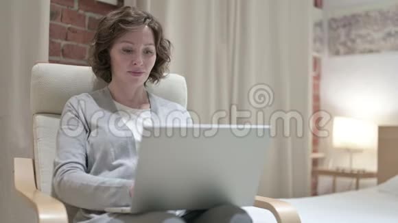老女人在卧室里用笔记本电脑视频的预览图