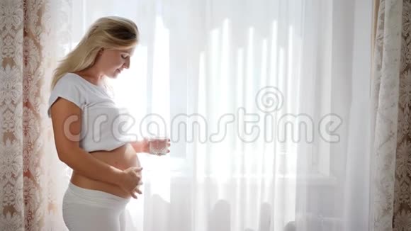 幸运的孕妇在靠近窗户的地方保持着玻璃纯净水视频的预览图