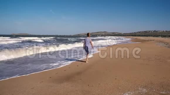 穿着裙子的苗条甜美女人光着脚在沙滩上散步背景是海浪和大海视频的预览图