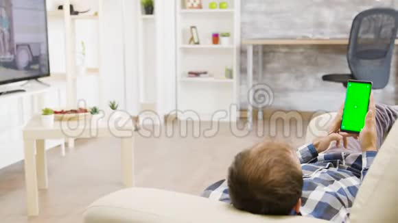 男性躺在沙发上看着绿色屏幕手机的视差镜头视频的预览图