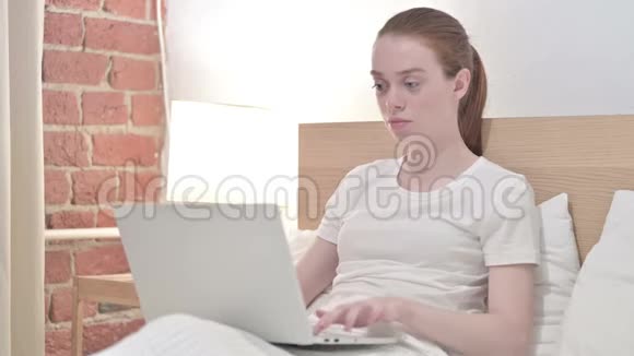 红发青年妇女在床上工作和打哈欠视频的预览图
