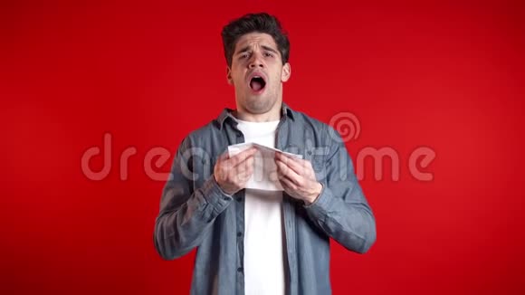 年轻人打喷嚏成纸巾在红工作室背景下孤立的家伙病了视频的预览图