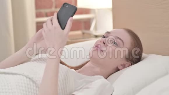 在床上使用智能手机的英俊红发青年妇女视频的预览图