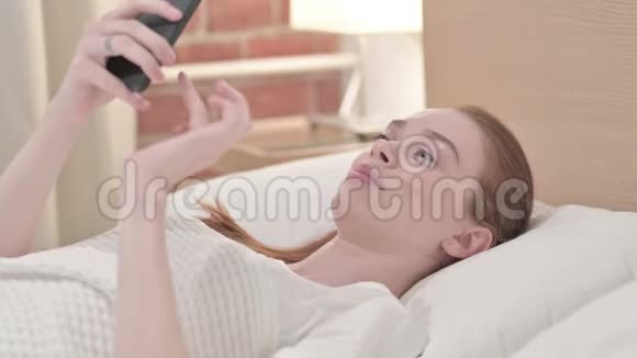 红头发青年妇女在床上讲智能电话视频的预览图