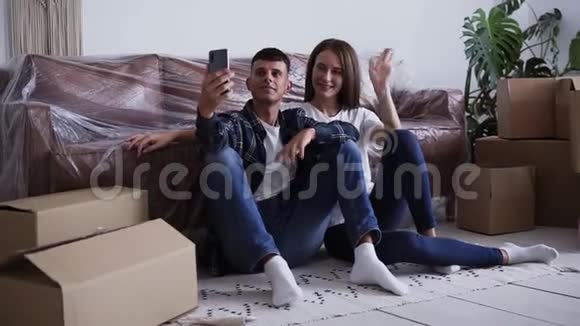 年轻快乐的白种人夫妇坐在他们的新房子的地板上自拍或给他们的朋友打视频电话视频的预览图