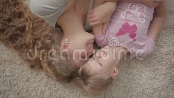 幸福的白种人母亲和她的小女儿躺在家里蓬松的地毯上女人和女孩休息视频的预览图
