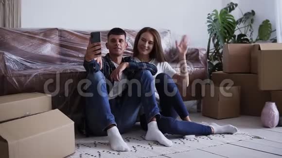 兴奋的白种人夫妇坐在他们的新房子的地板上自拍或给他们的朋友打视频电话视频的预览图
