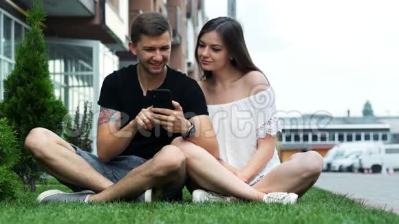快乐的一对夫妻在草地上玩手机上网购物冲浪视频的预览图