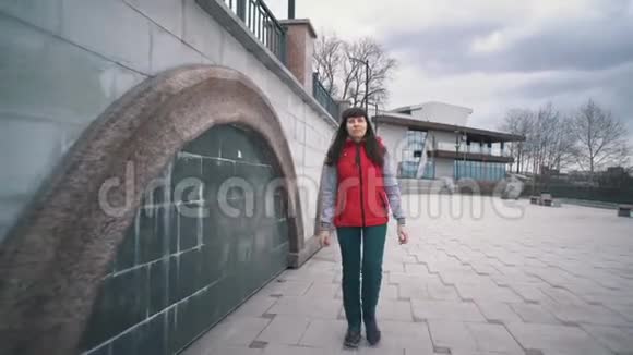 阴天穿着无袖红色夹克的女孩走在大理石墙旁边视频的预览图