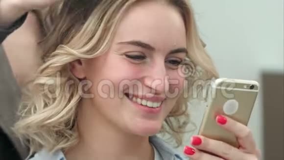 美丽的女人在美容院使用智能手机同时还有发型视频的预览图