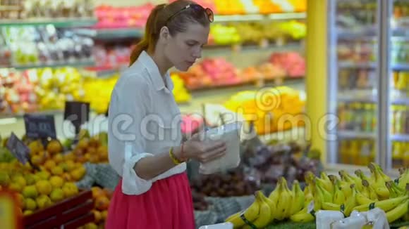 年轻的美国女购物者选择香蕉站在杂货店视频的预览图
