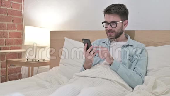 床上使用智能手机的年轻男性设计师视频的预览图