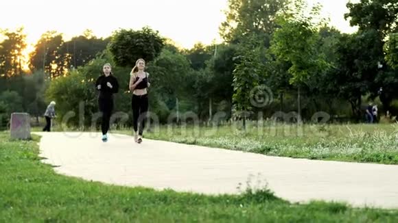 两个年轻的健身妇女一起在公园的夕阳下奔跑视频的预览图