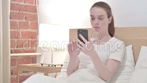 红发美女在床上使用智能手机视频的预览图