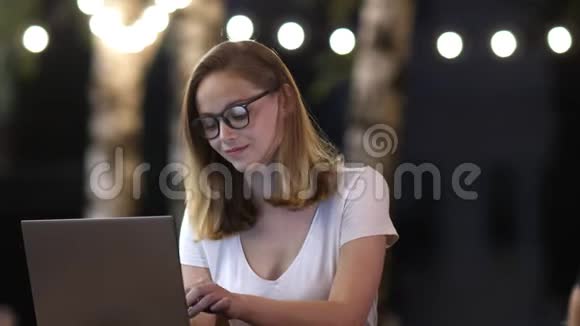 年轻的休闲商务女性戴着带笔记本电脑的眼镜晚上在外面工作视频的预览图