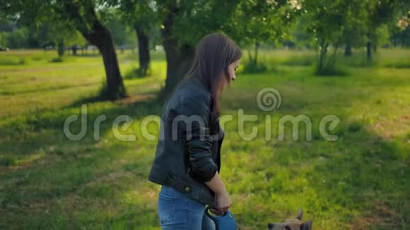 一个20岁的小女孩牵着她的狗在公园里用皮带散步视频的预览图