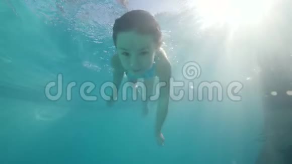 小女孩在游泳池里潜水在水下游泳经过相机看着它视频的预览图