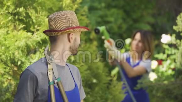 英俊的年轻农民穿着蓝色长袍站在前景而他的妻子在背景中浇水男性和女性视频的预览图