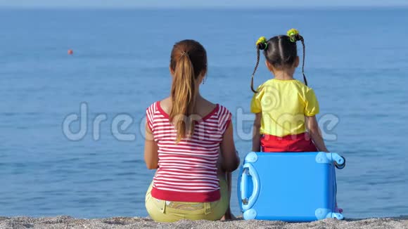 小可爱的女孩和她穿着五颜六色衣服的妈妈坐在海滩上视频的预览图