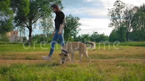 在公园里一个穿着皮夹克牛仔裤带着她的狗的漂亮女孩被广泛的稳定镜头拍到了视频的预览图