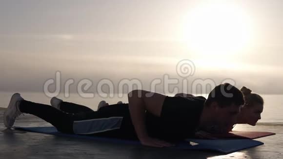 高加索男人和女人练习瑜伽或伸展后在前面的海洋或海洋上的瑜伽垫上午视频的预览图