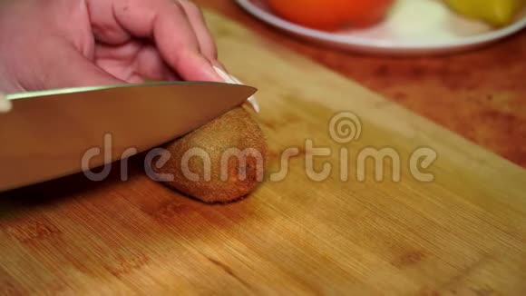 木制木板上的女孩用刀切开一种成熟多汁的维他命青猕猴桃视频的预览图