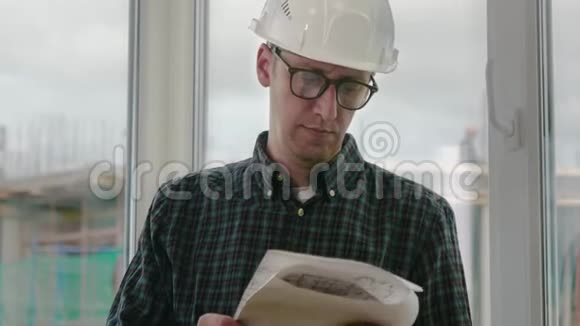 建筑工程师戴安全帽在窗框背景上看蓝图纸施工图视频的预览图