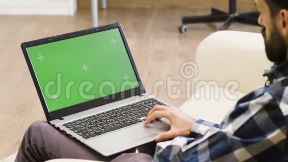 沙发上的男人看着绿色屏幕笔记本电脑视频的预览图