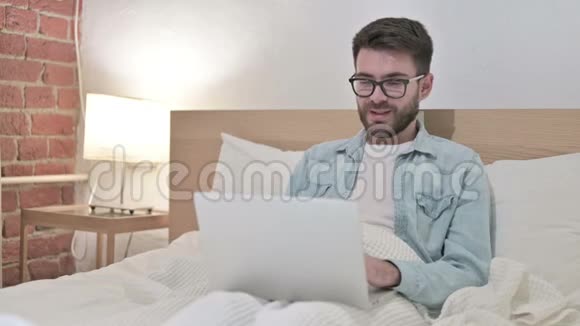 年轻男性设计师在床上玩手机聊天视频的预览图